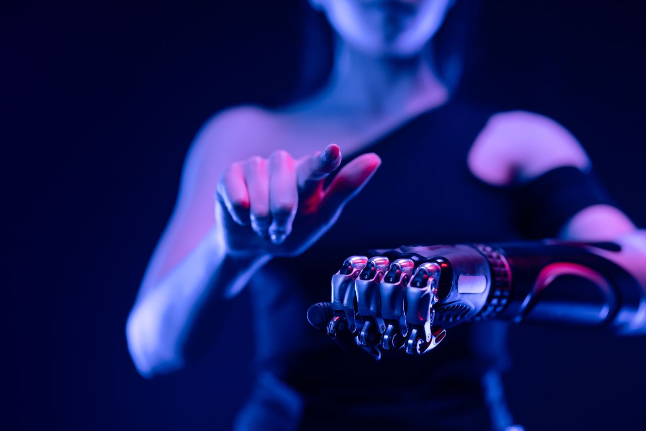 about-bg Close-up of a robotic hand with a woman pointing, showcasing advanced prosthetic technology.